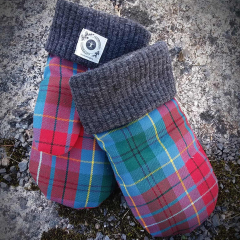 Pair of tartan mittens with grey cuffs on a stone surface