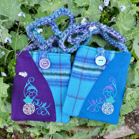 Two fabric pouches with tartan patterns and decorative designs on a green leaf background