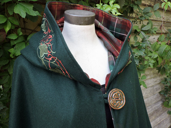 Green cloak with PEI tartan and embroidered details on a mannequin against a natural background