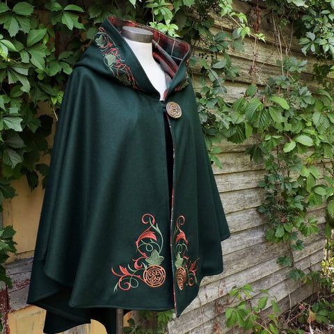 Green cape with PEI tartan and embroidery on a mannequin against a leafy background