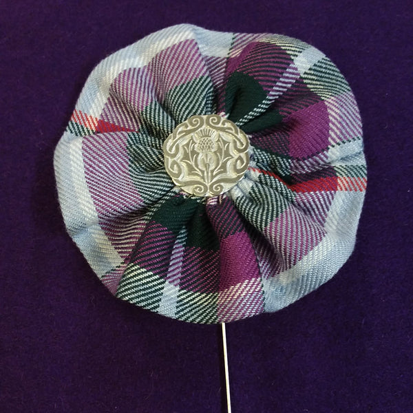 Plaid fabric flower brooch with gold center and pin on a purple background